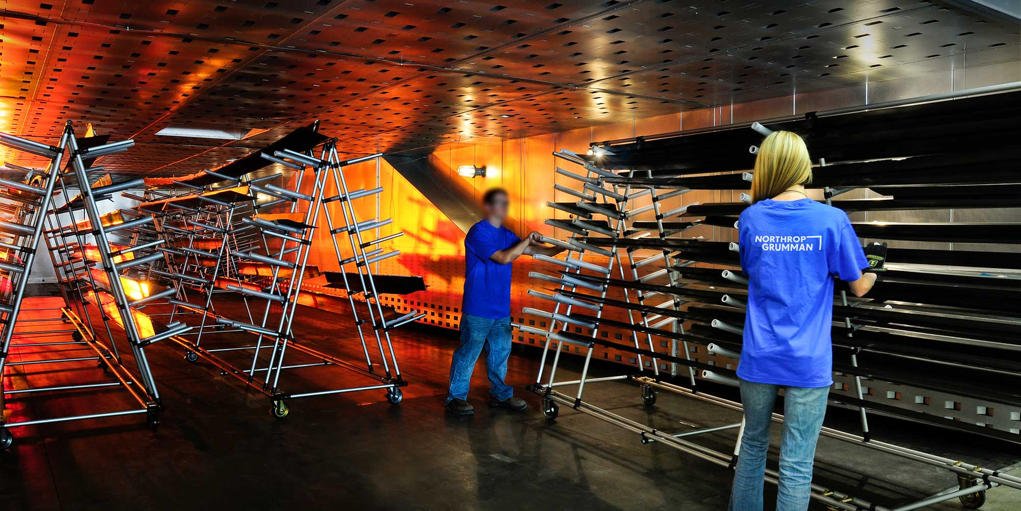 Two people putting metal aircraft pieces on racks