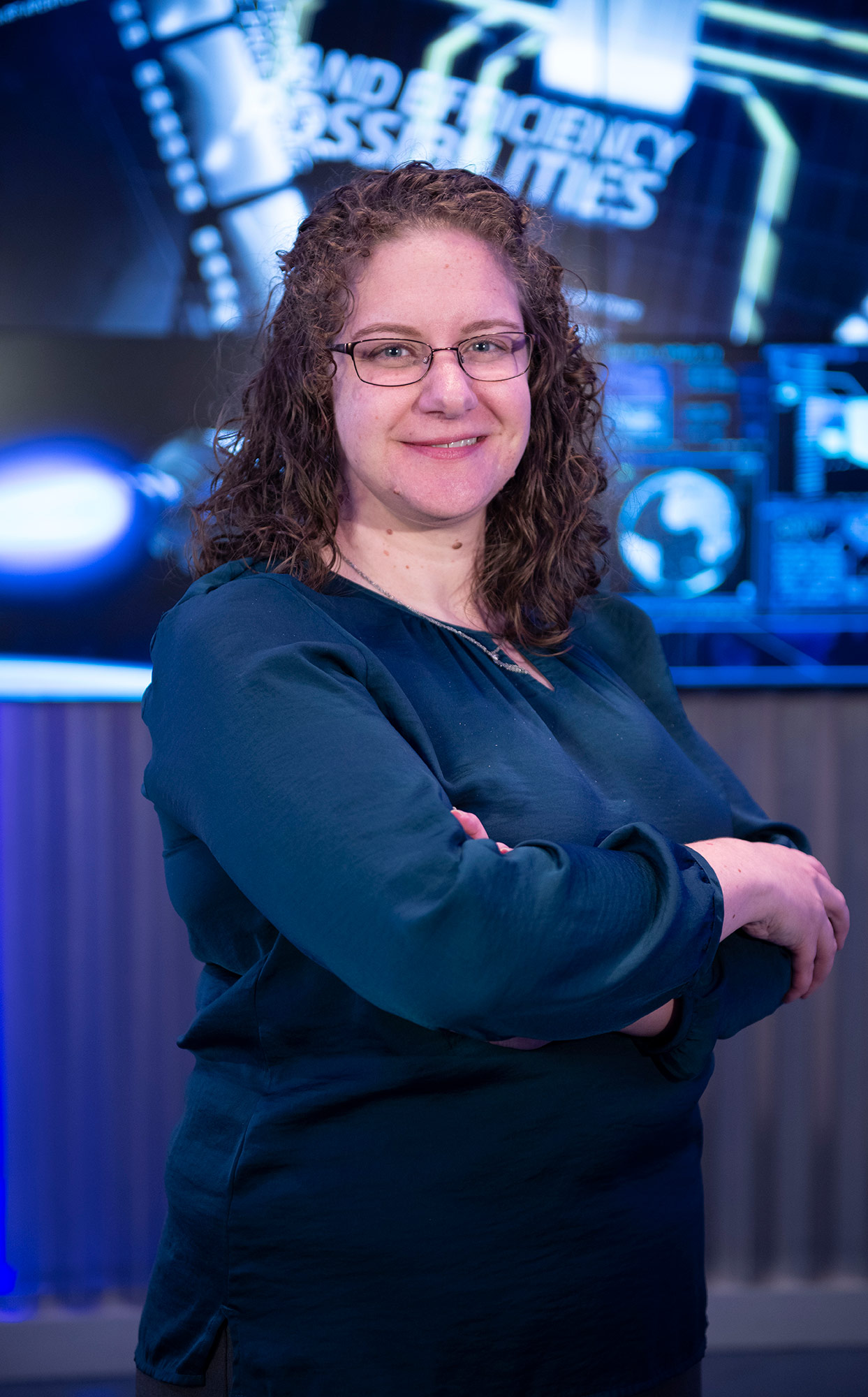 A white woman stands with her arms crossed in front of a computerized background