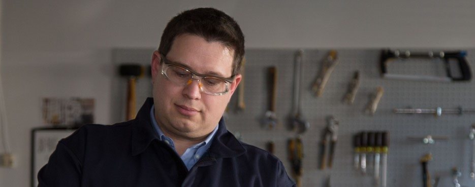 White man wearing safety goggles works in workshop