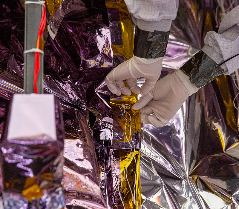 two hands carefully applying materials to spacecraft