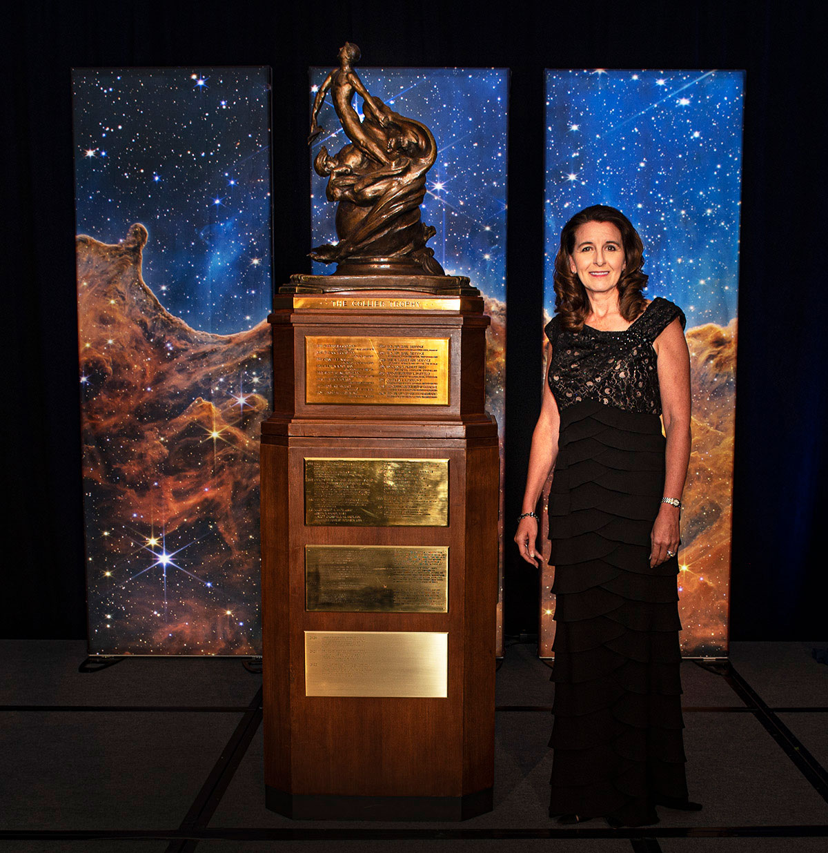 woman in gown standing next to large trophy