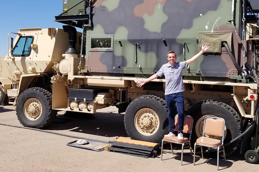 Young man standing in front of large camoflauged truck