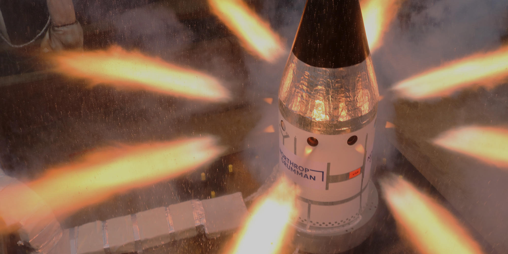Rocket motor testing in action. Vertical capsule with flames shooting out of the sides.