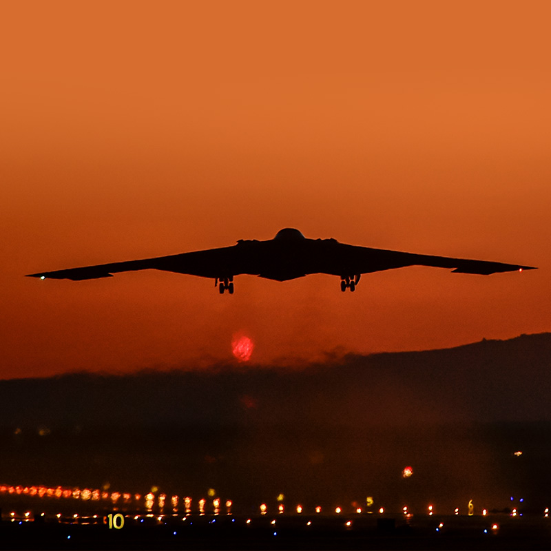 b-2 bomber flying into a red sky at sunset